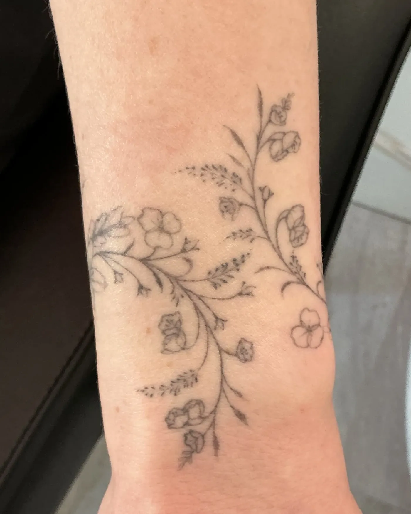 A fine line floral tattoo wrapping a wrist, before laser removal