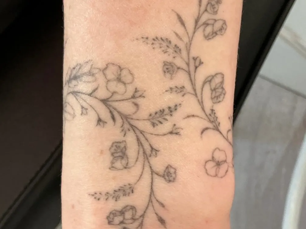 A fine line floral tattoo wrapping a wrist, before laser removal